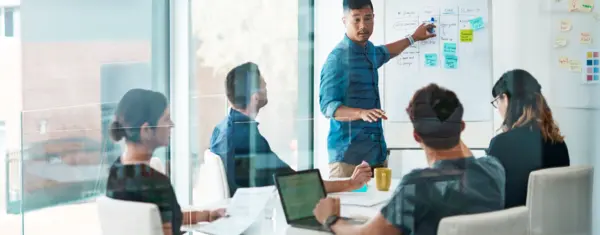 Frau zeigt anderen Personen etwas auf dem Monitor